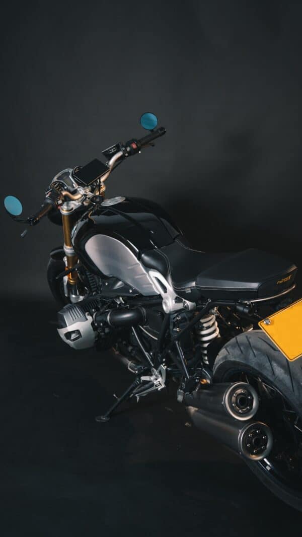 A sleek modern motorcycle with a combination of black and metallic colors, showcased against a dark background. The bike features a prominent golden front suspension, twin rear exhausts, and blue-tinted side mirrors.
