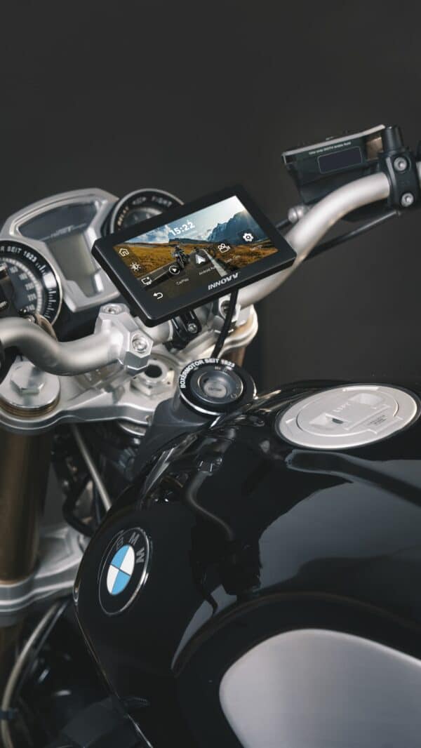 A close-up view of a BMW motorcycle's handlebar area, featuring a mounted GPS device with a display screen showing a map on a clear day, the BMW emblem on the fuel tank, and part of the dashboard gauges.